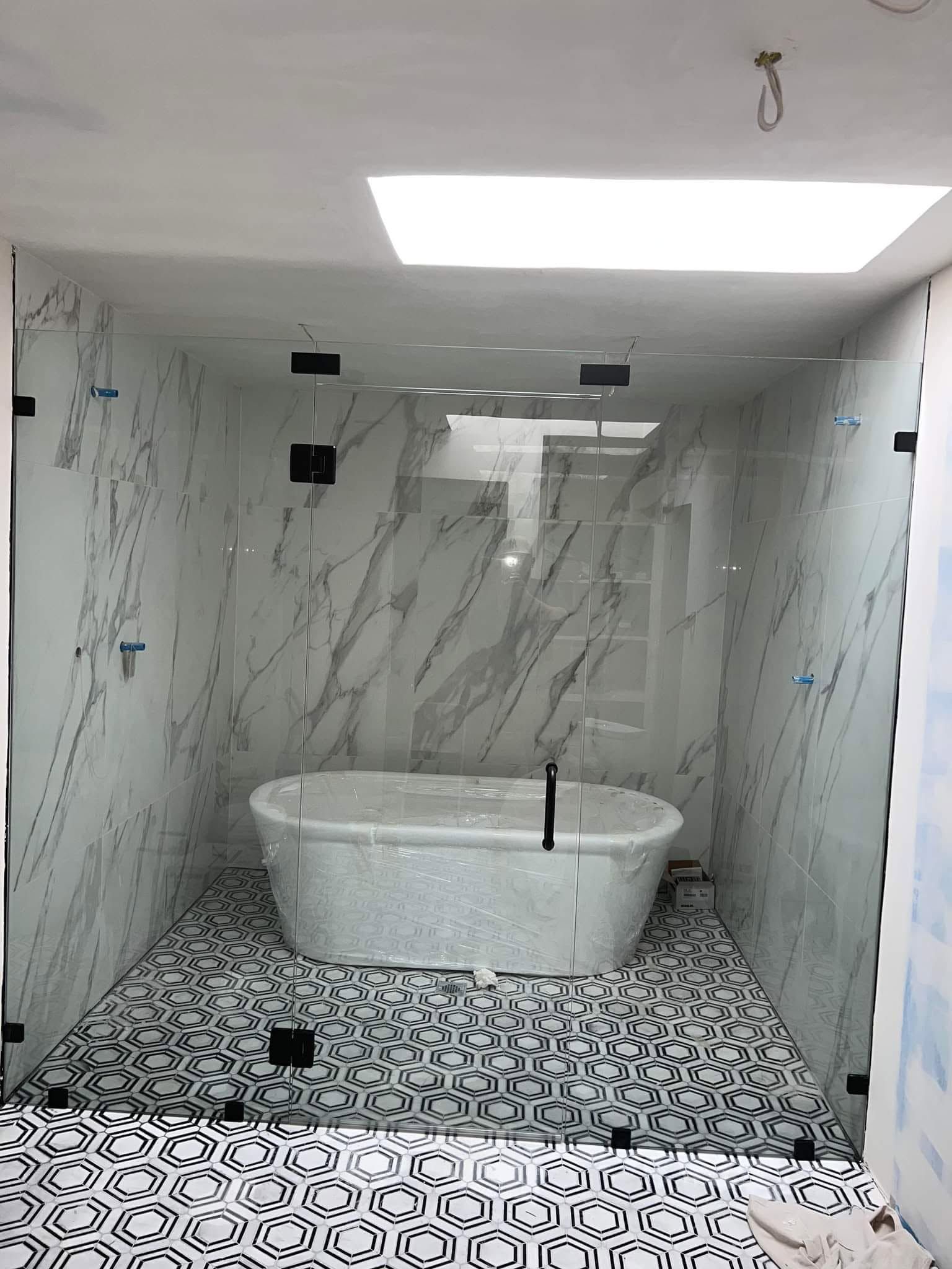 Modern bathroom with marble walls, mosaic tile floor, soaking tub, and a skylight above the shower area