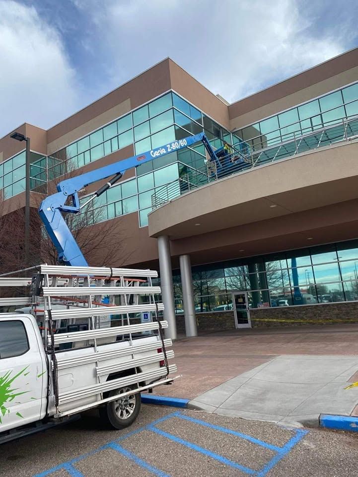Blue boom lift and work truck outside a modern glass office building under cloudy skies