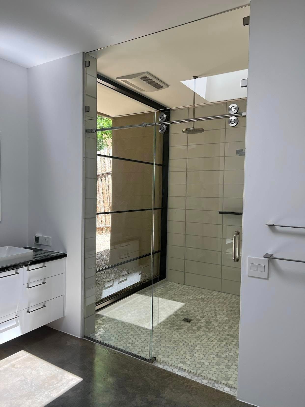 Modern bathroom with glass shower, white vanity, and tiled floor lit by sunlight