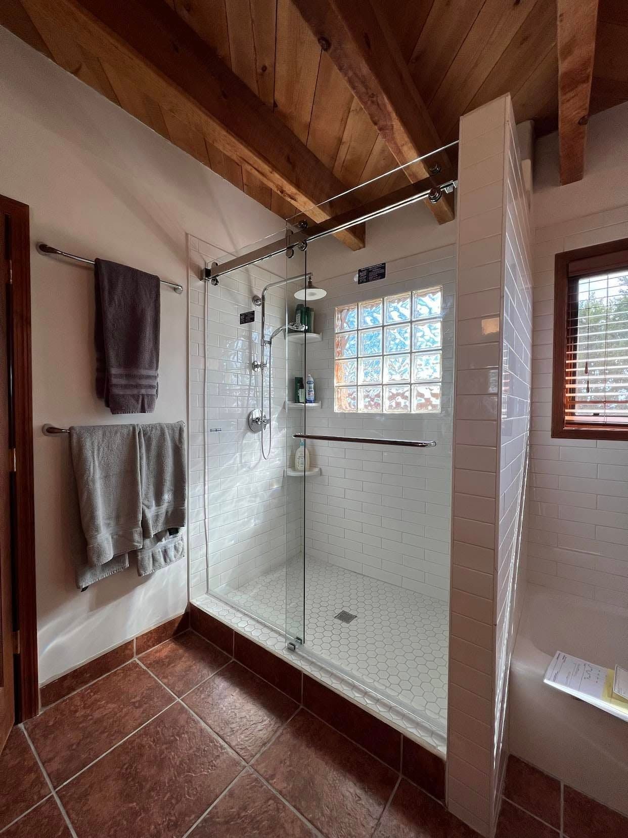 Bathroom with glass shower, terracotta tile floor, wood ceiling, and towels hanging on the wall