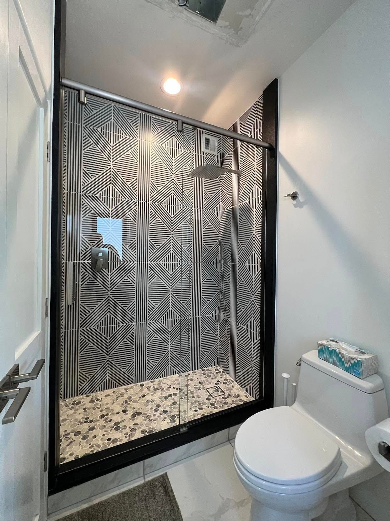 Modern bathroom with a glass-enclosed shower, black-and-white patterned tile, and a toilet in the foreground