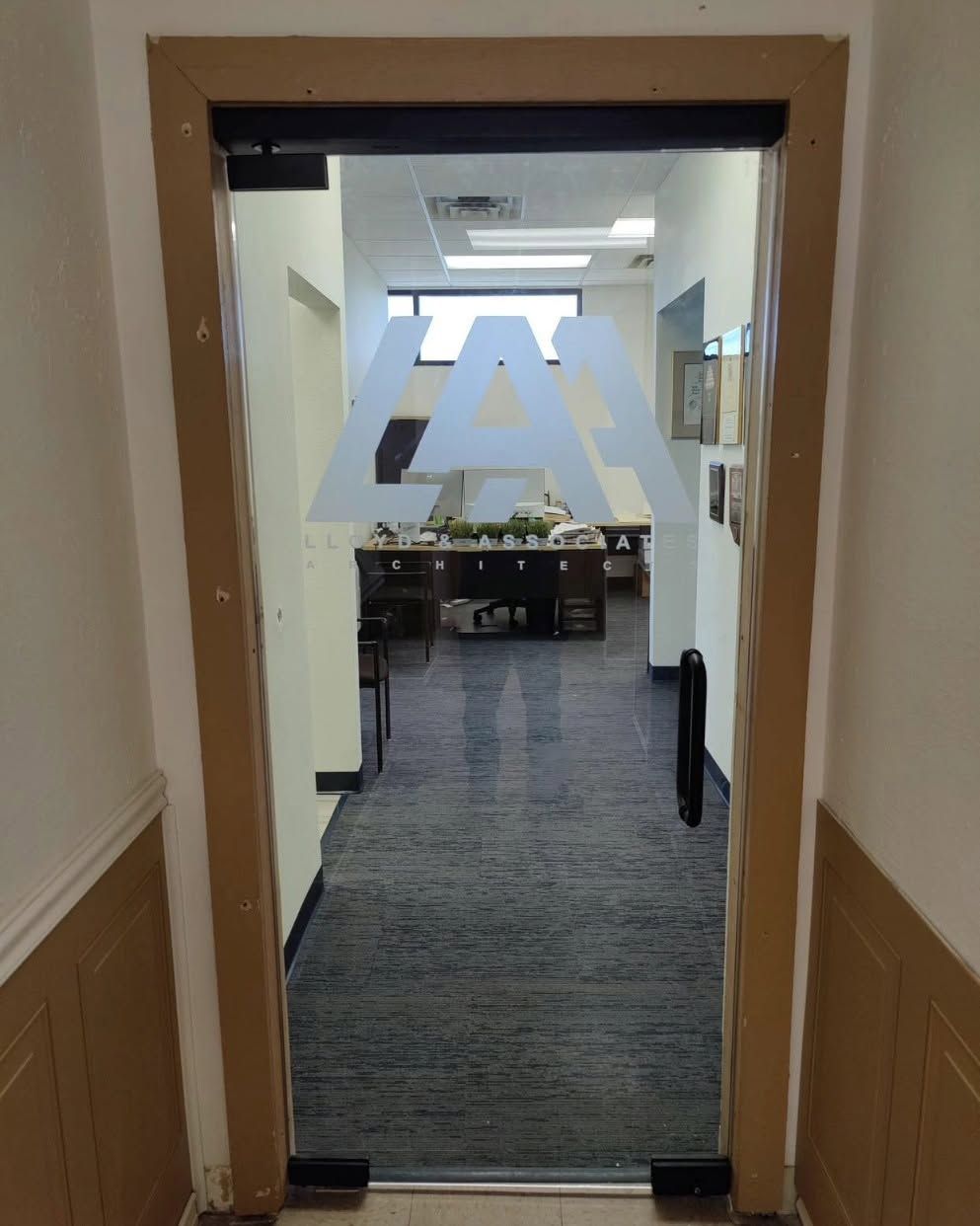 Hallway doorway opening into an office with desks and chairs, seen from a carpeted corridor