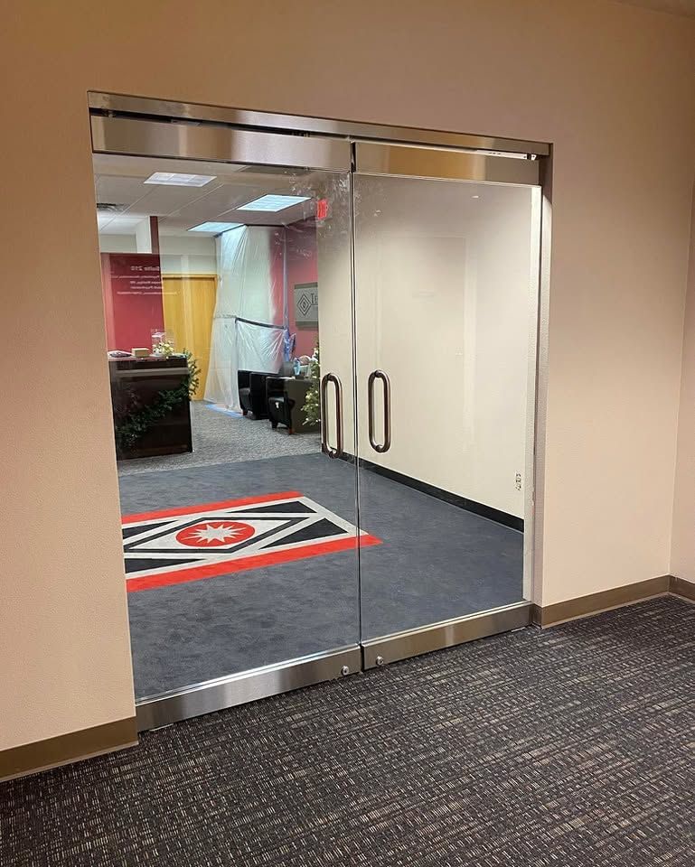 Glass double doors leading to an office lobby with carpeted hallway and red-and-black floor sign