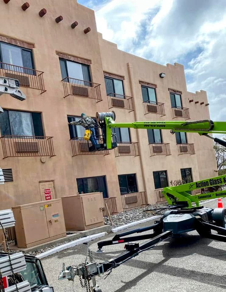 Green boom lift raising a worker beside a tan apartment building with cardboard boxes below