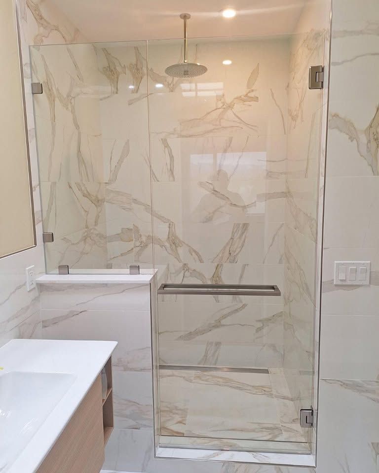 Modern bathroom with marble-look shower enclosure, glass door, and vanity sink.