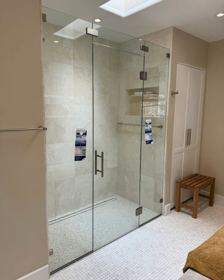 Glass-enclosed walk-in shower with white tile, beige walls, and a small wooden bench nearby