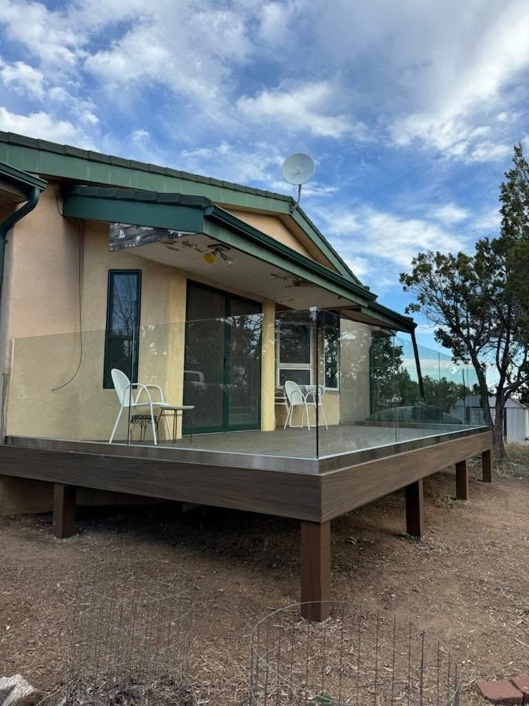 Small beige house with green roof and glass porch on a raised wooden deck under a cloudy sky