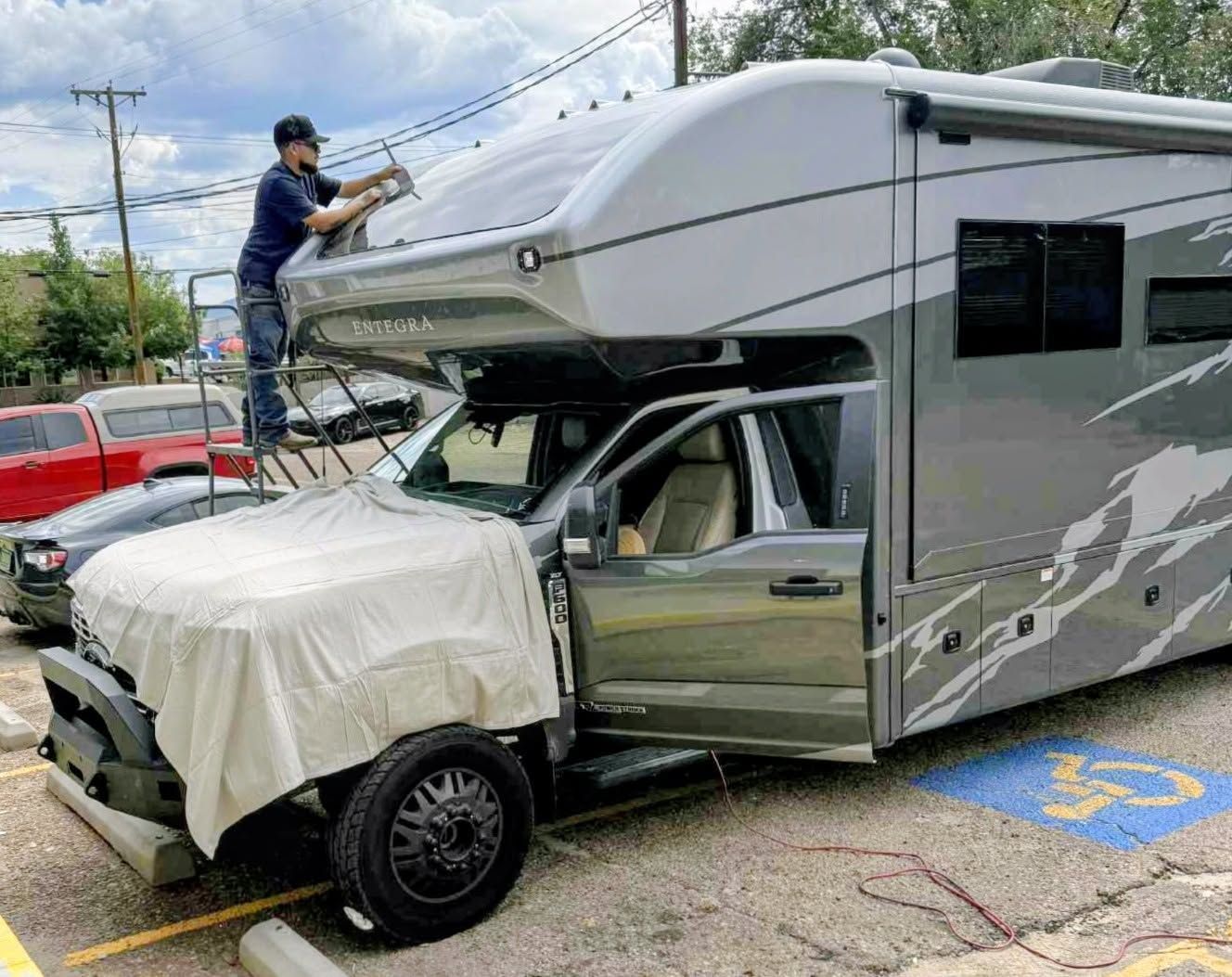 RVs colliding in a parking lot, with one person standing on the damaged motorhome roof.