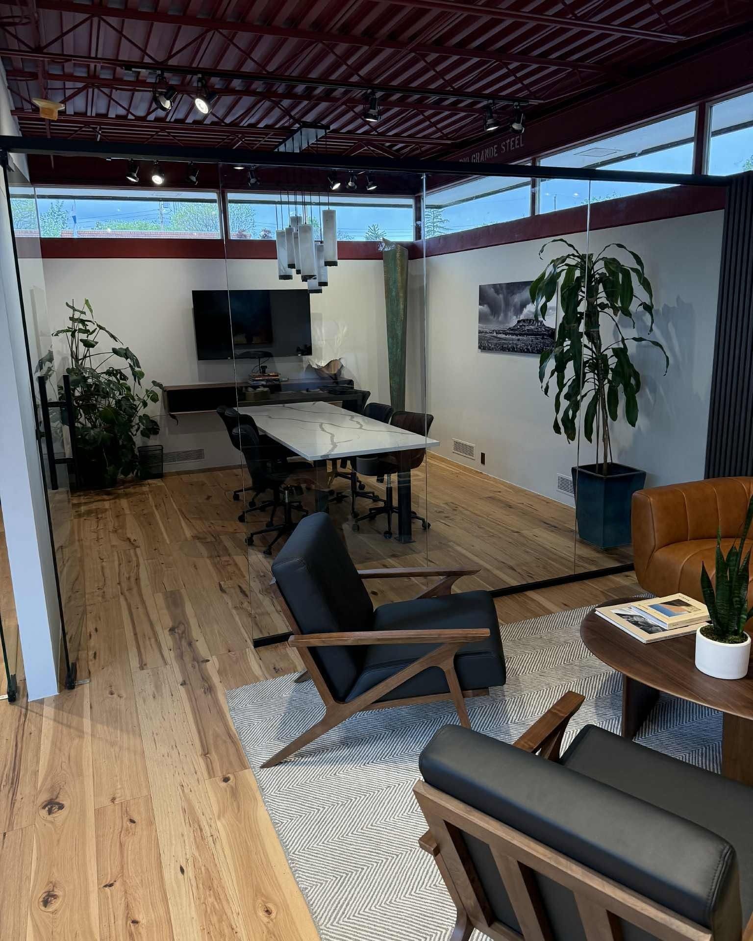 Modern open-plan lounge with wood floors, black chairs, a table, plants, and a TV area under exposed beams