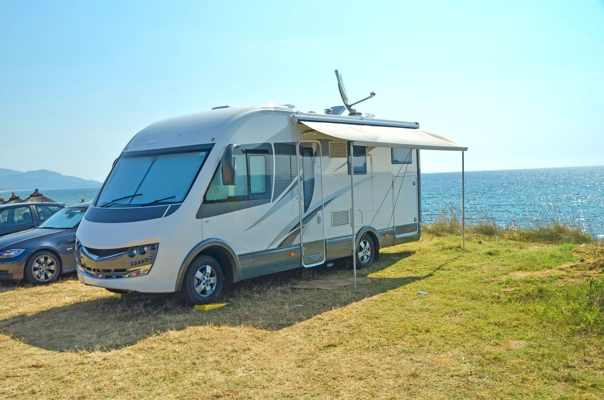Silver RV parked on grassy seaside cliff under a clear blue sky