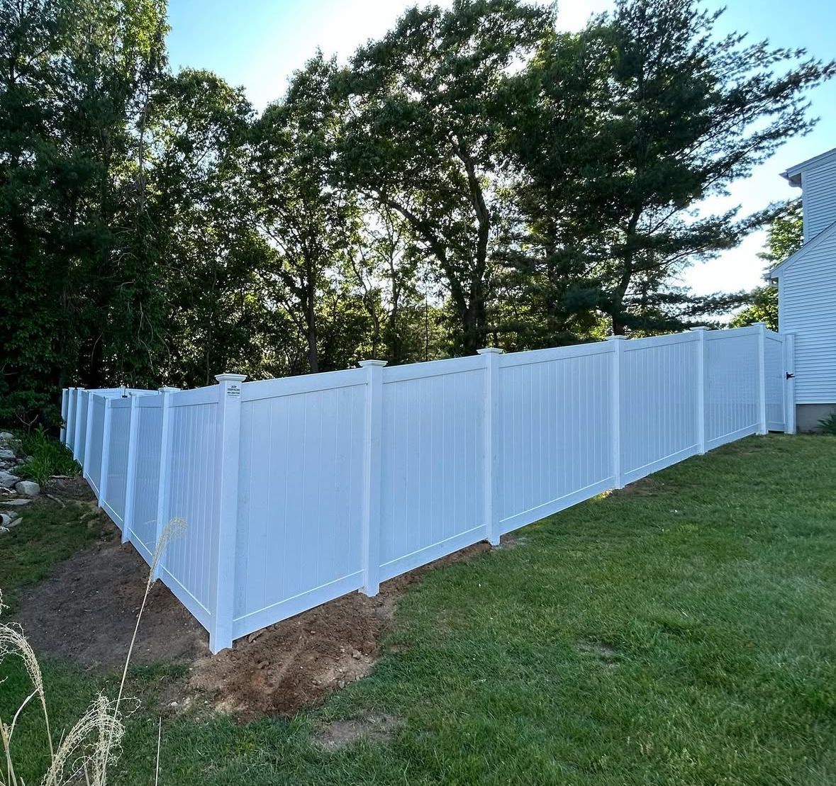 A white vinyl fence is sitting in the middle of a lush green yard.