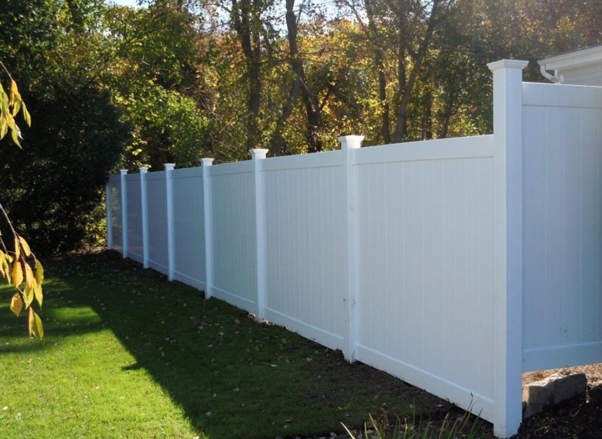 A white fence surrounds a lush green yard with trees in the background.