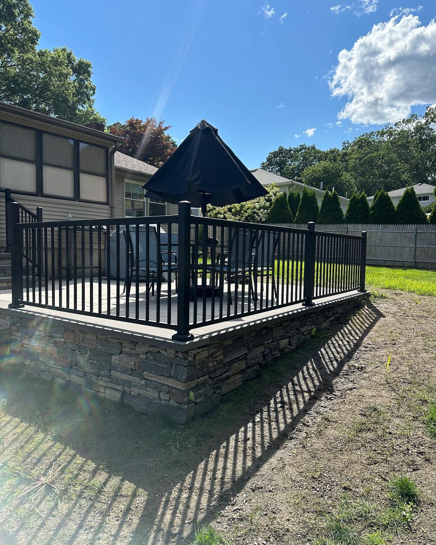 A deck with a black umbrella and chairs on it.