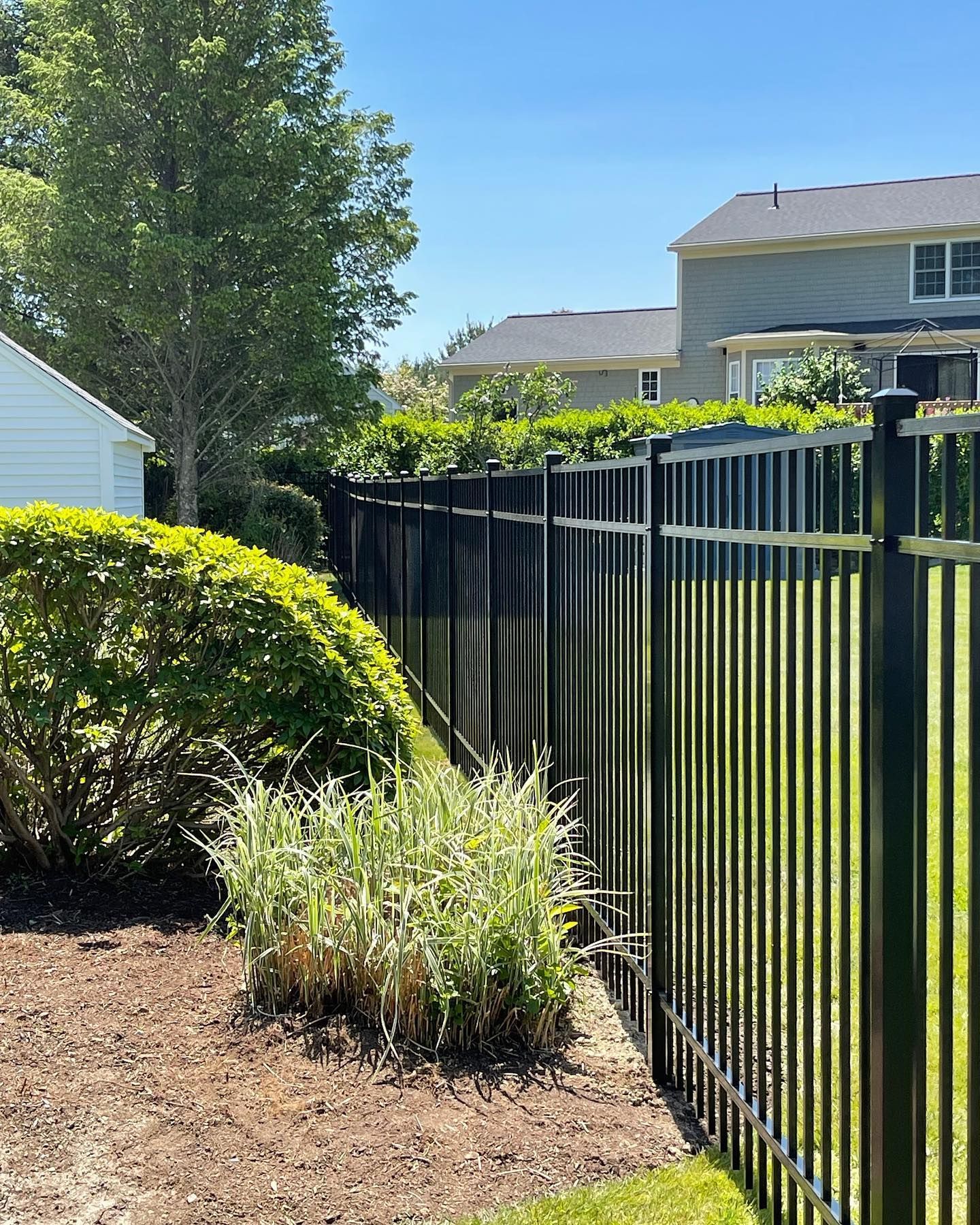 A black fence surrounds a lush green yard in front of a house.