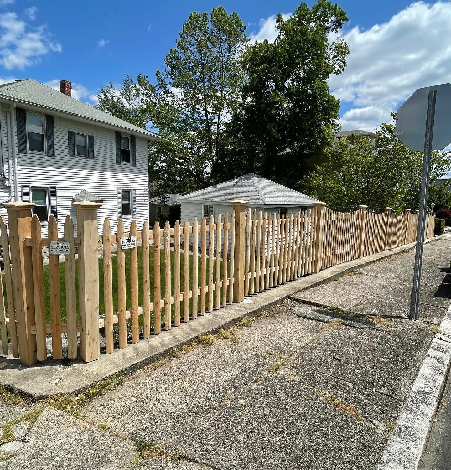 A wooden picket fence along the side of a road next to a house.