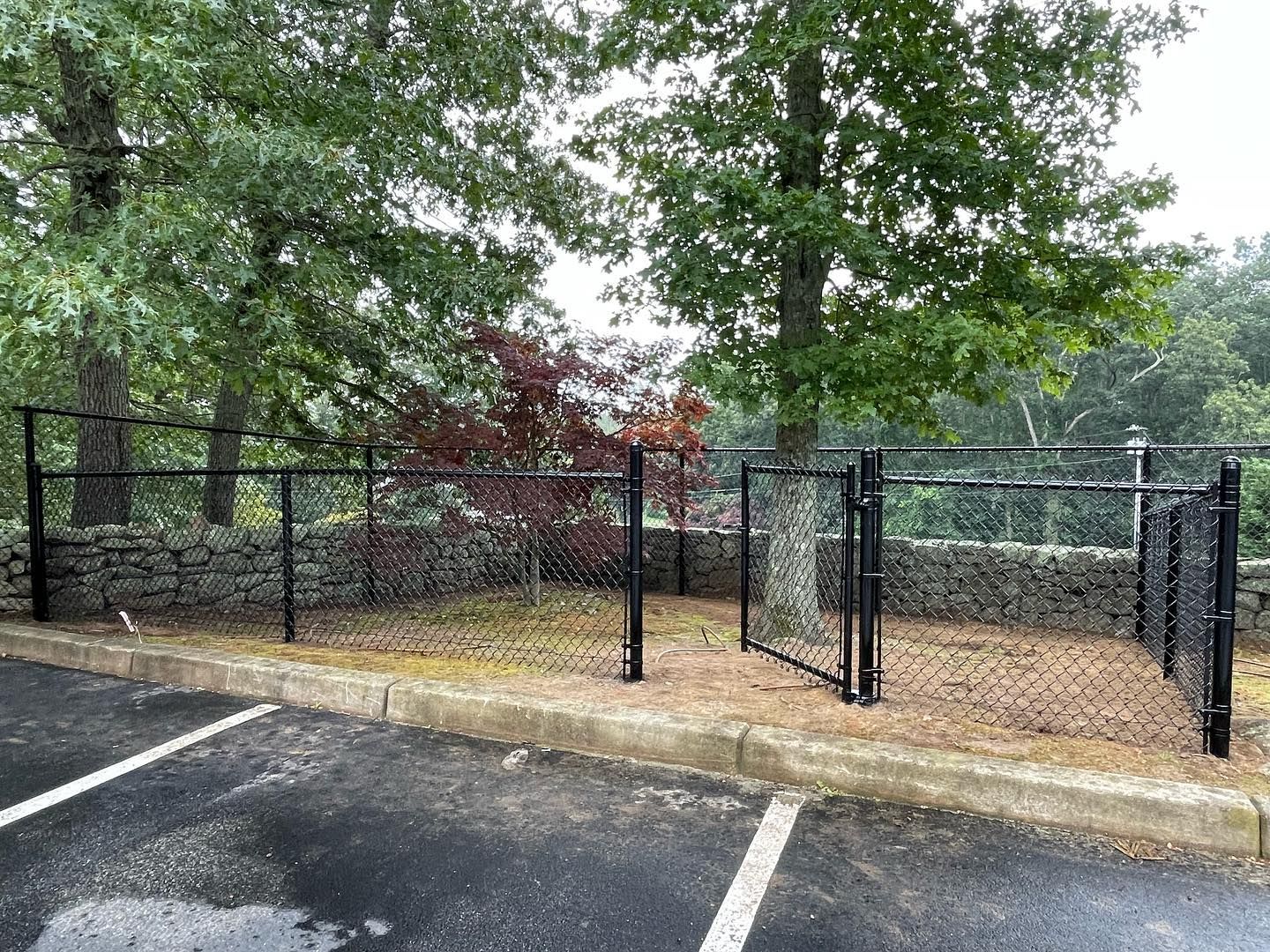 A chain link fence is surrounding a parking lot with trees in the background.