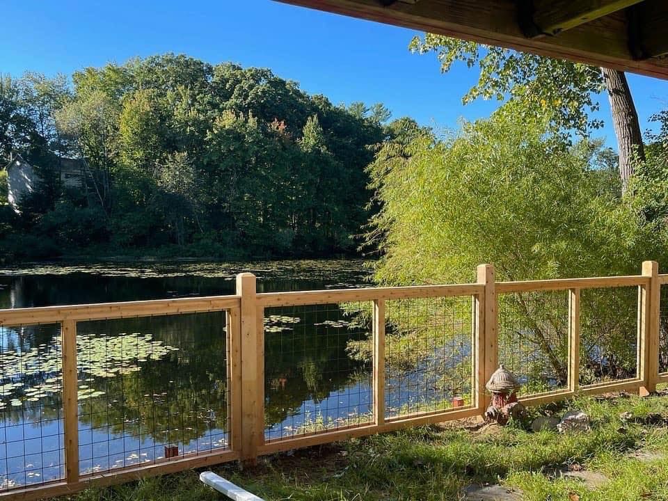 A wooden fence surrounds a lake with trees in the background.