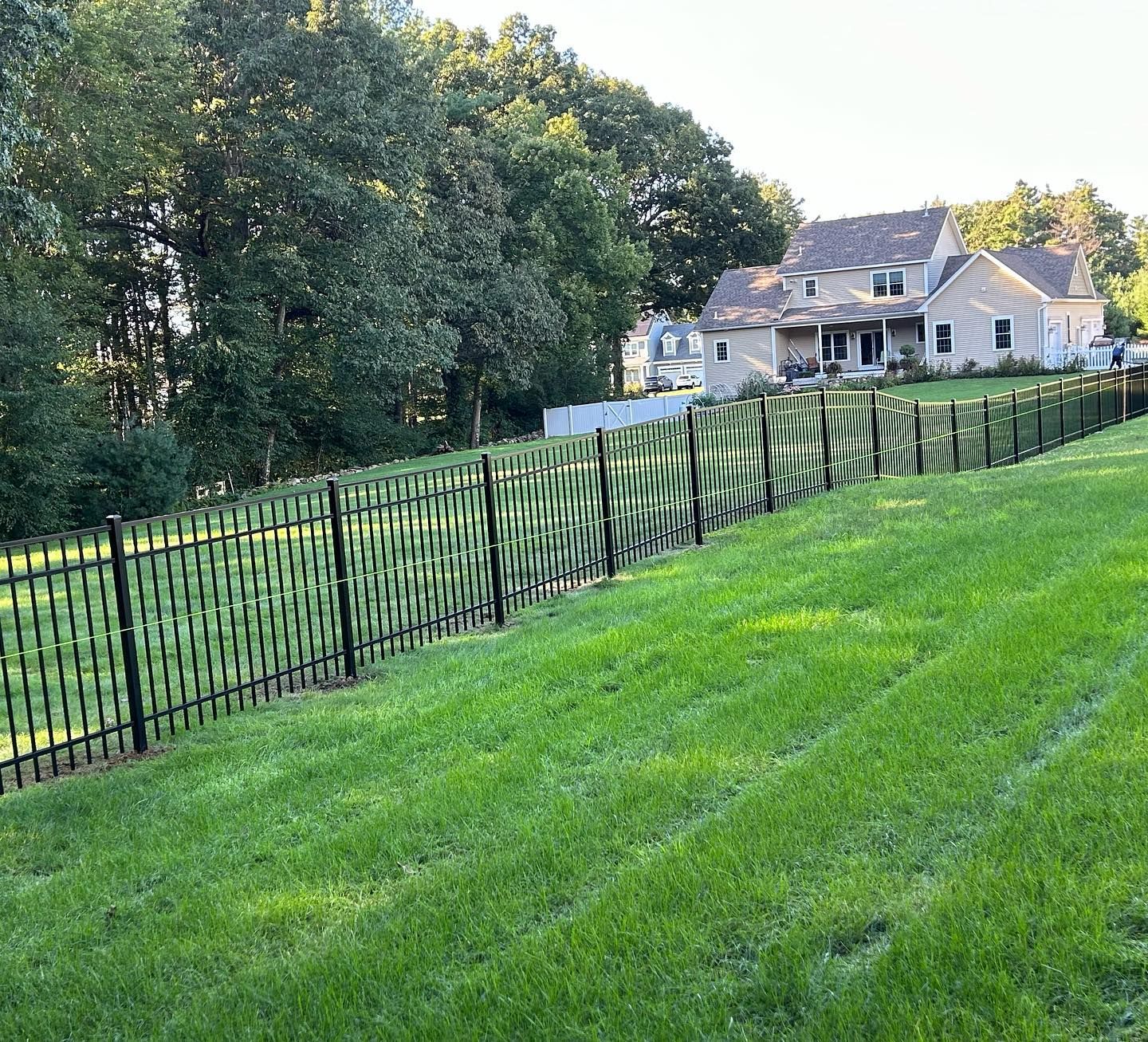 A fence surrounds a lush green field with a house in the background.