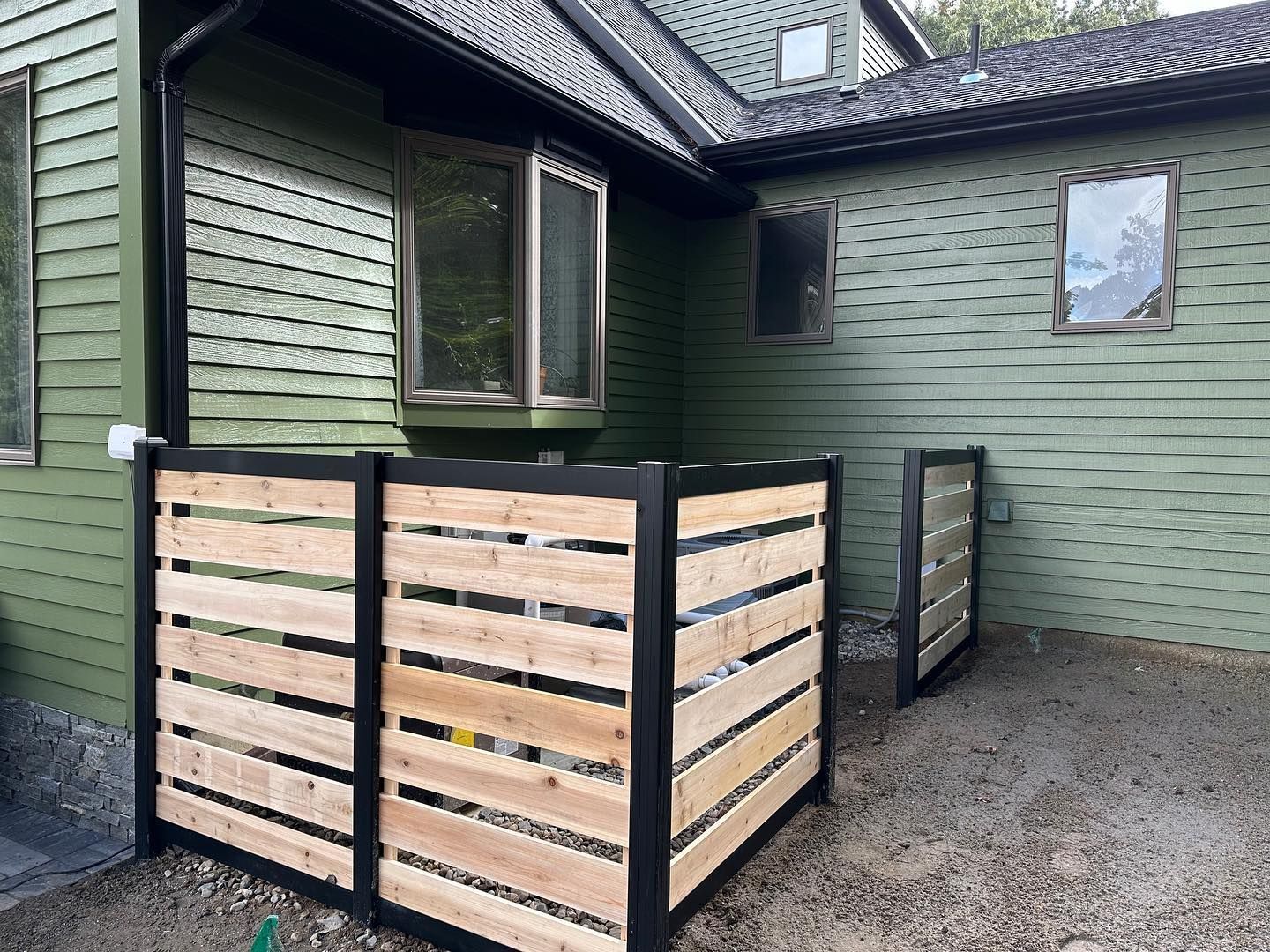 A wooden fence is in front of a green house.