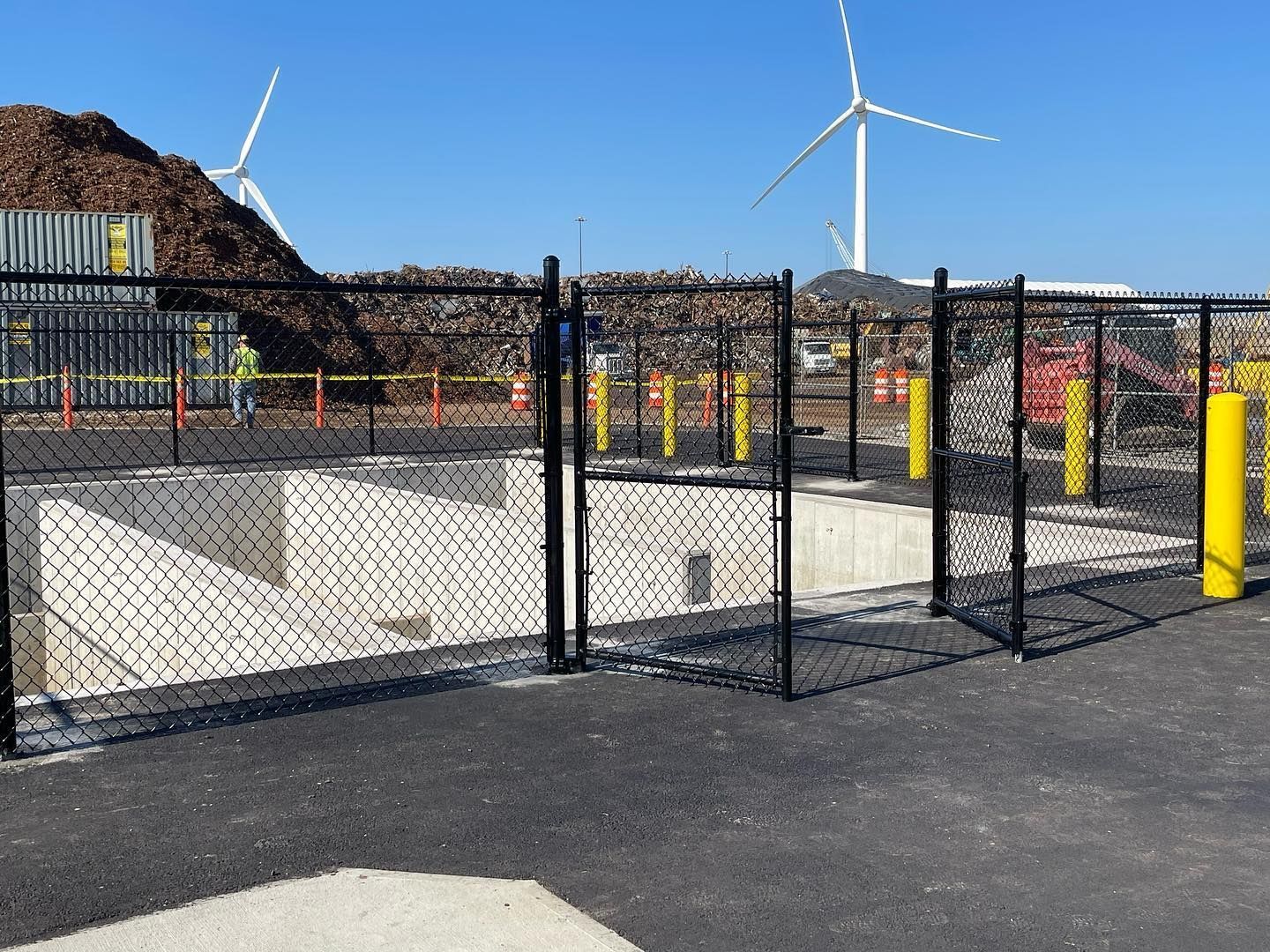 A chain link fence surrounds a construction site with windmills in the background.