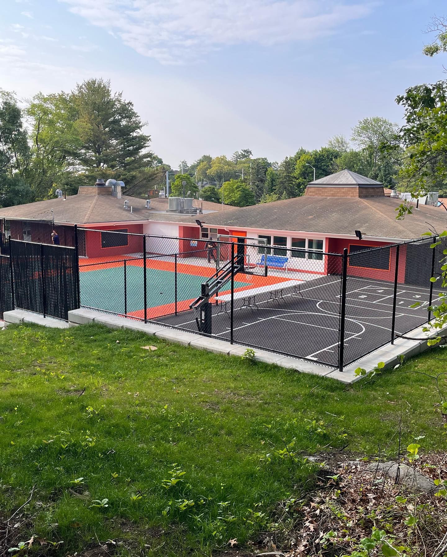 A fence surrounds a basketball court in front of a house.