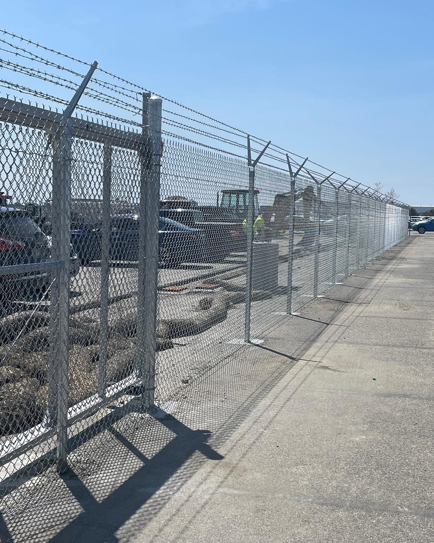 A chain link fence with barbed wire surrounding a parking lot.