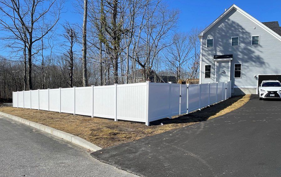 A white car is parked in front of a house with a white fence.