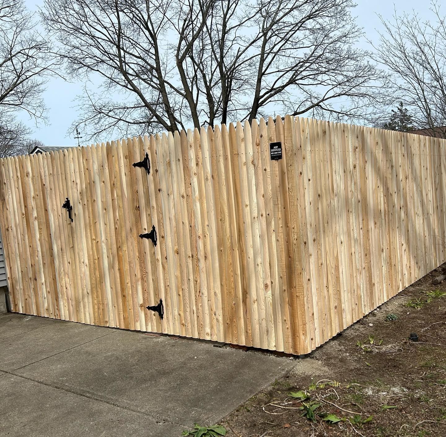 A wooden fence is sitting next to a sidewalk and trees.