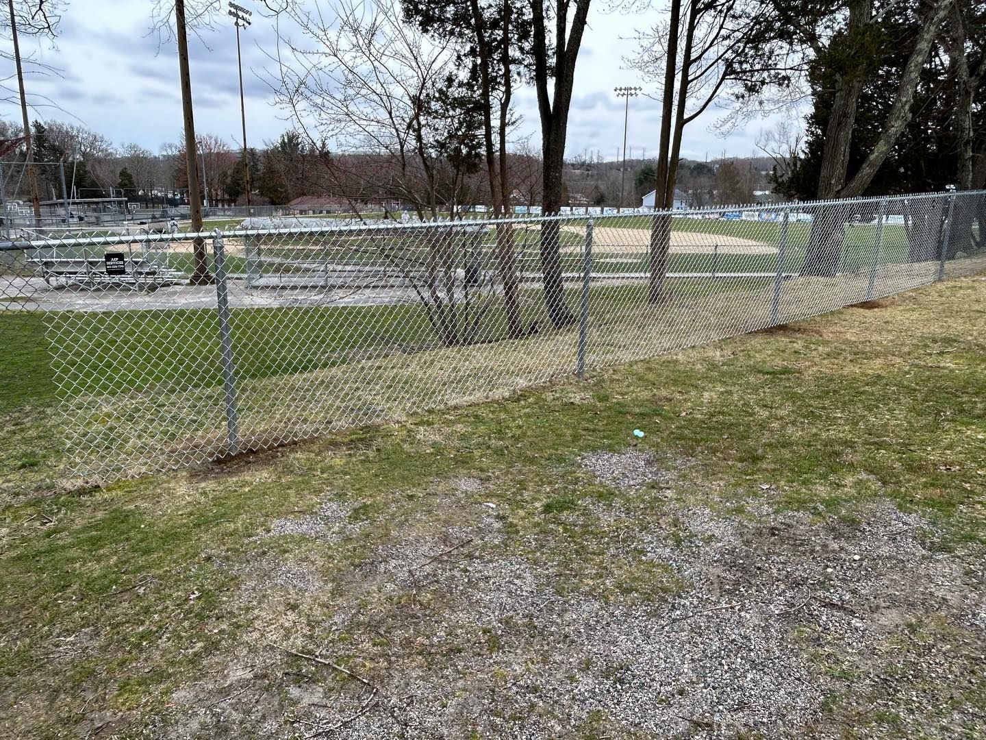 A chain link fence surrounds a baseball field in a park.