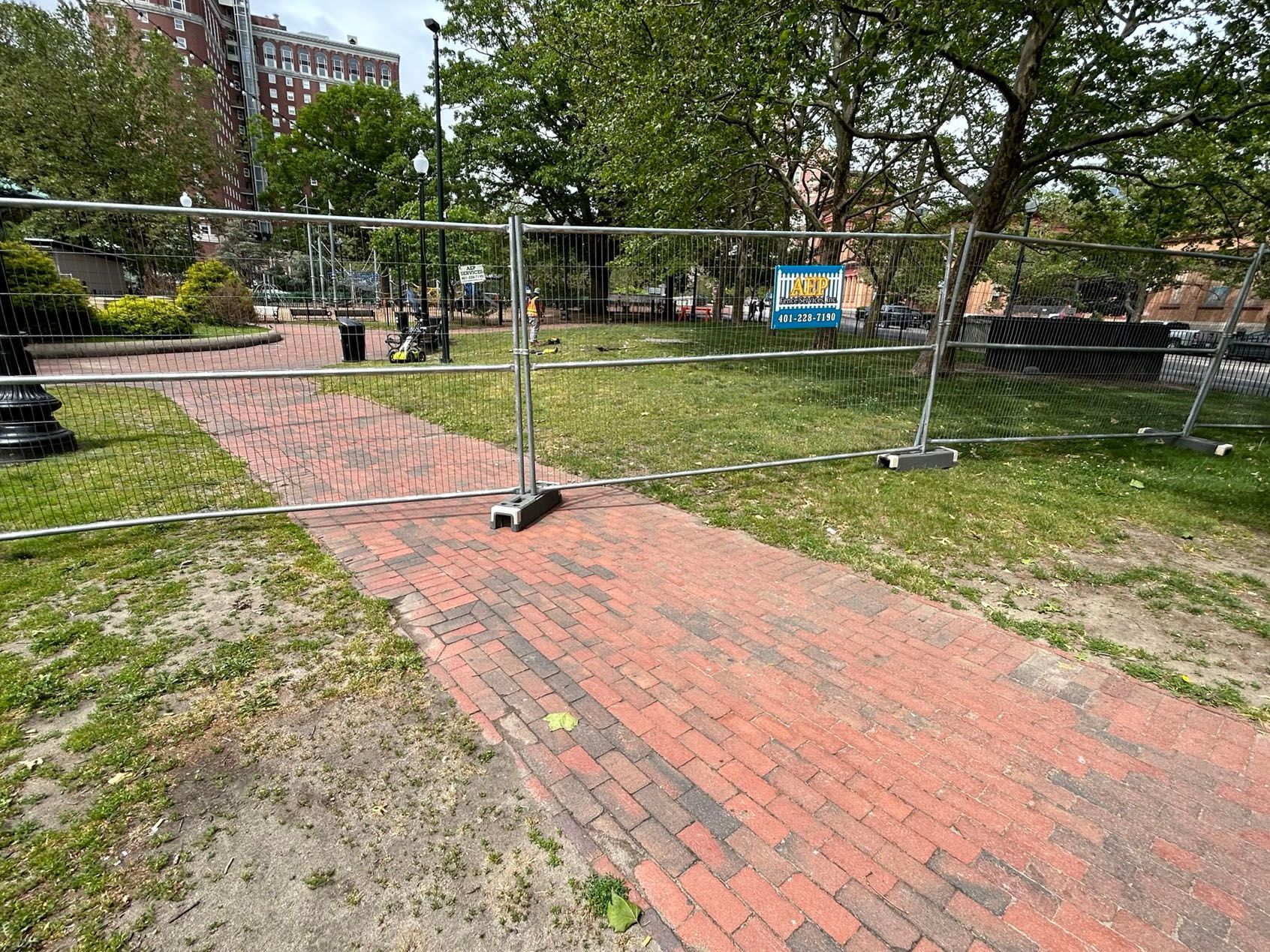 A fence is surrounding a brick walkway in a park.