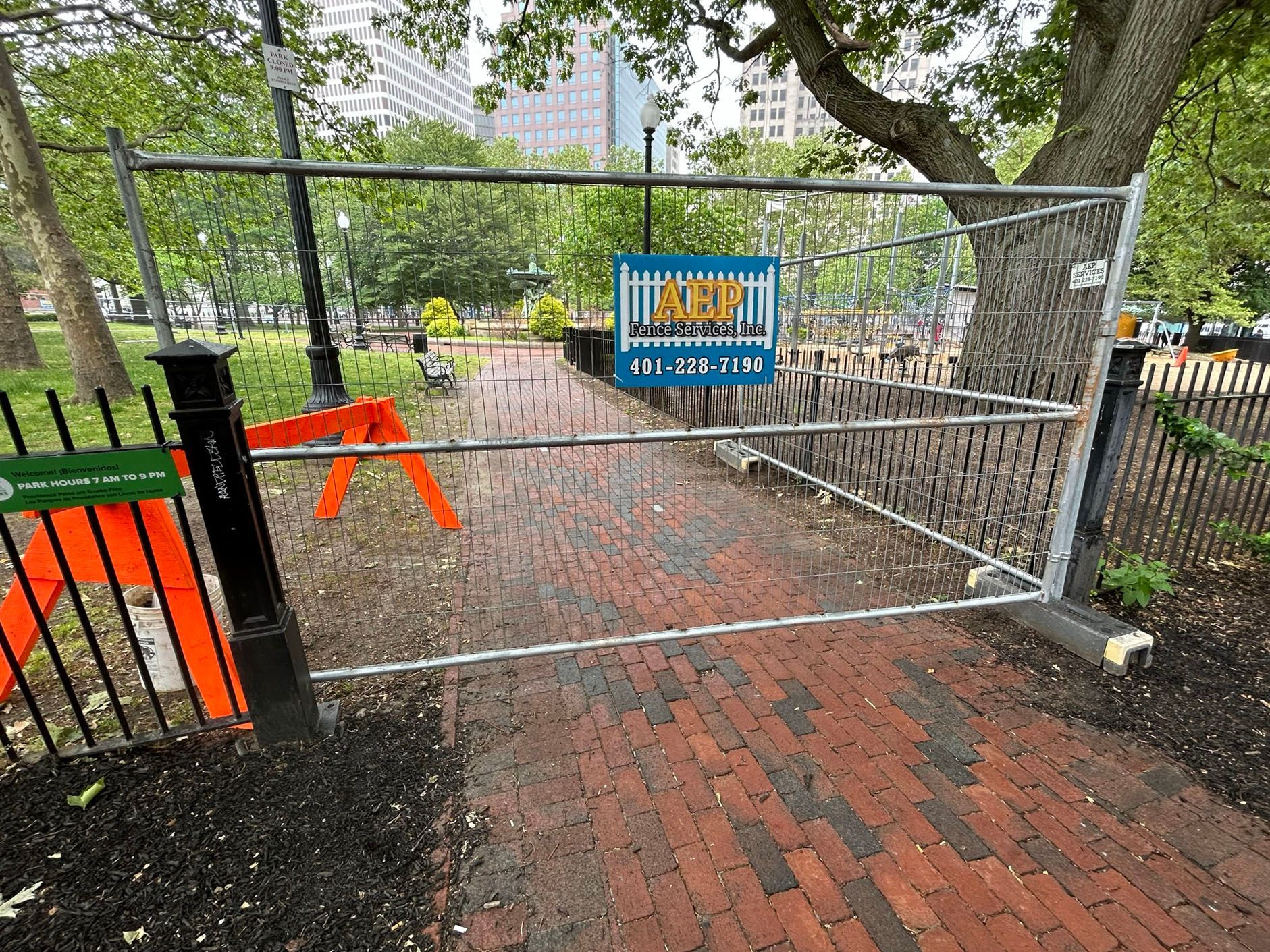 A fence with a sign on it is blocking a path in a park.