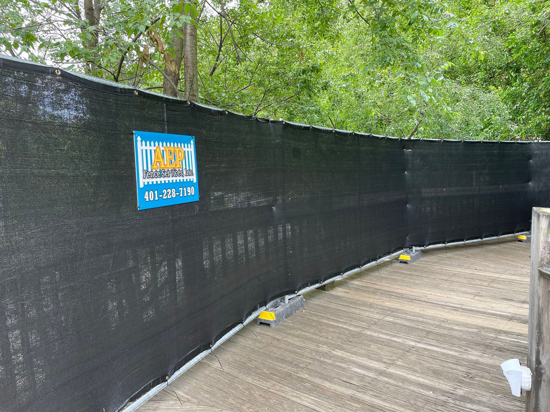 A black fence with a blue sign on it is surrounded by trees.
