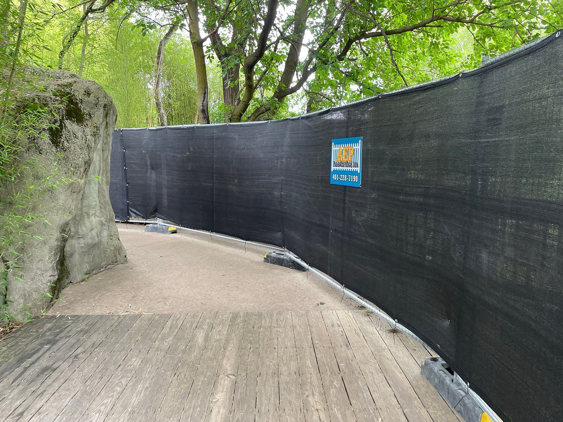 A black fence surrounds a wooden path in the woods.
