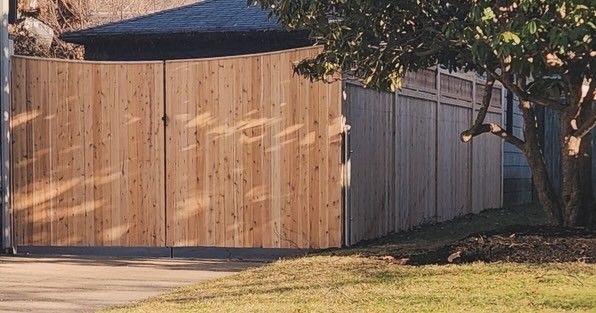 Wooden privacy fence and gate in front of a house. A tree stands on the right.