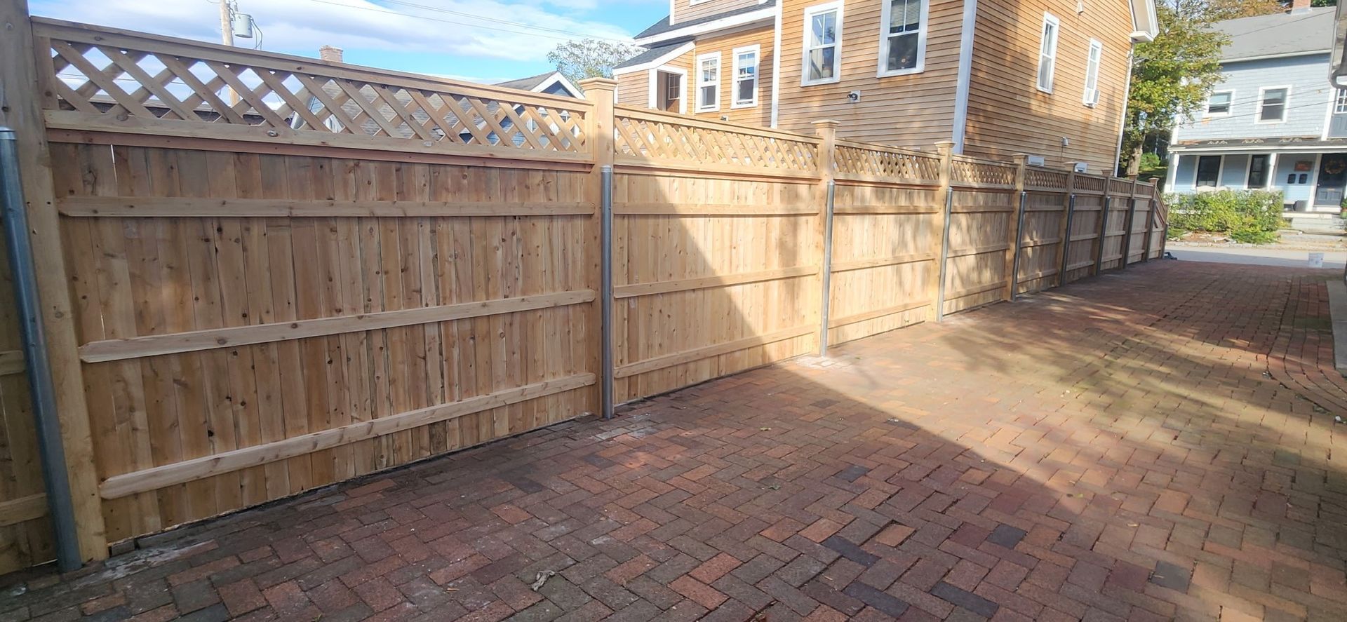 A brick patio next to a wooden fence surrounding buildings.