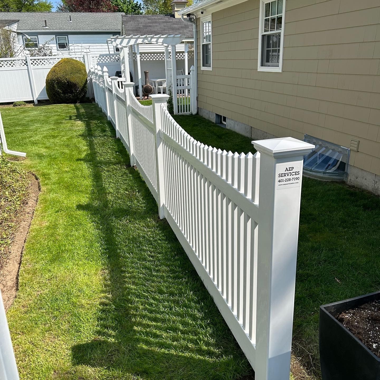 White picket fence in a green yard next to a beige house, sunny day.