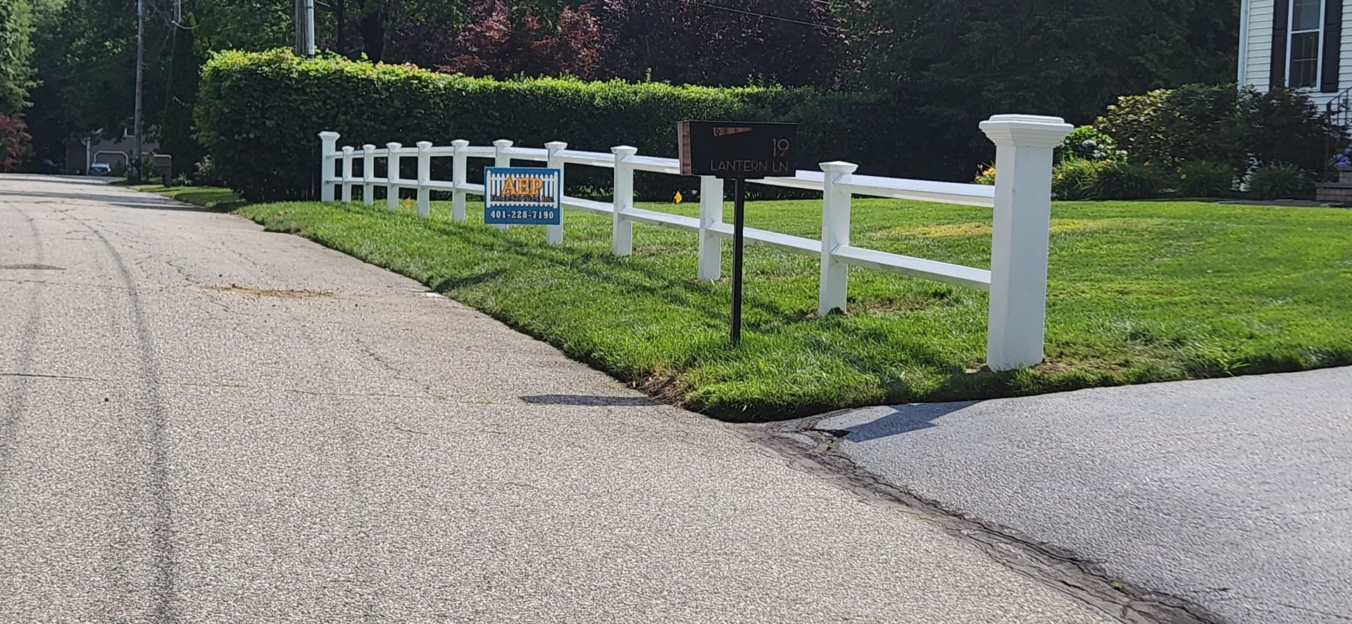 White fence lining a grassy roadside beside a paved path on a sunny day