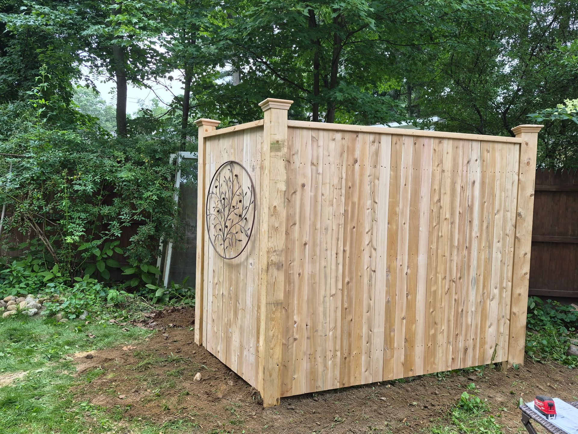 Wooden outdoor shed with a carved circular design, set in a leafy backyard.