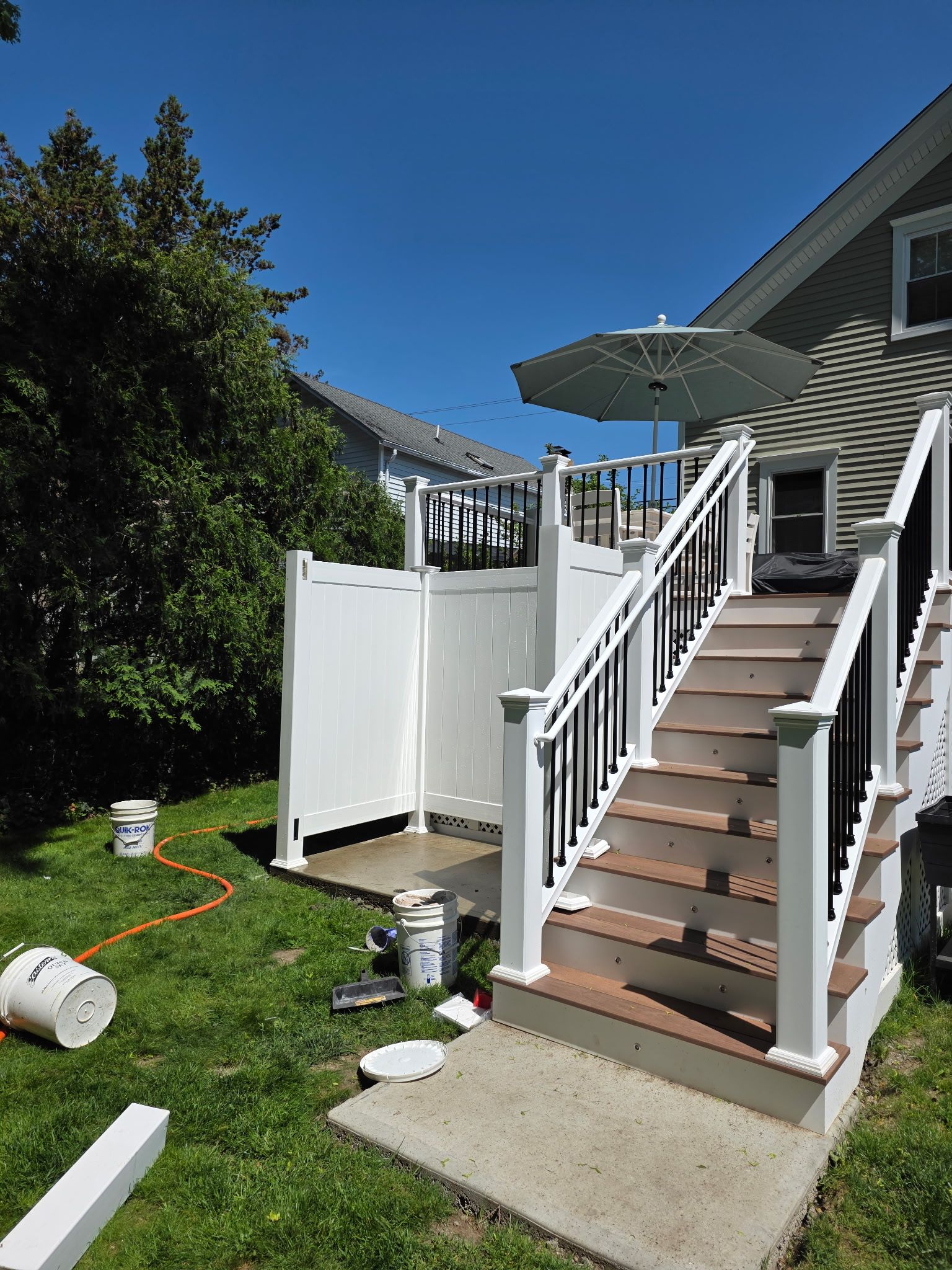 Backyard deck stairs with white railing and patio umbrella beside a white privacy fence