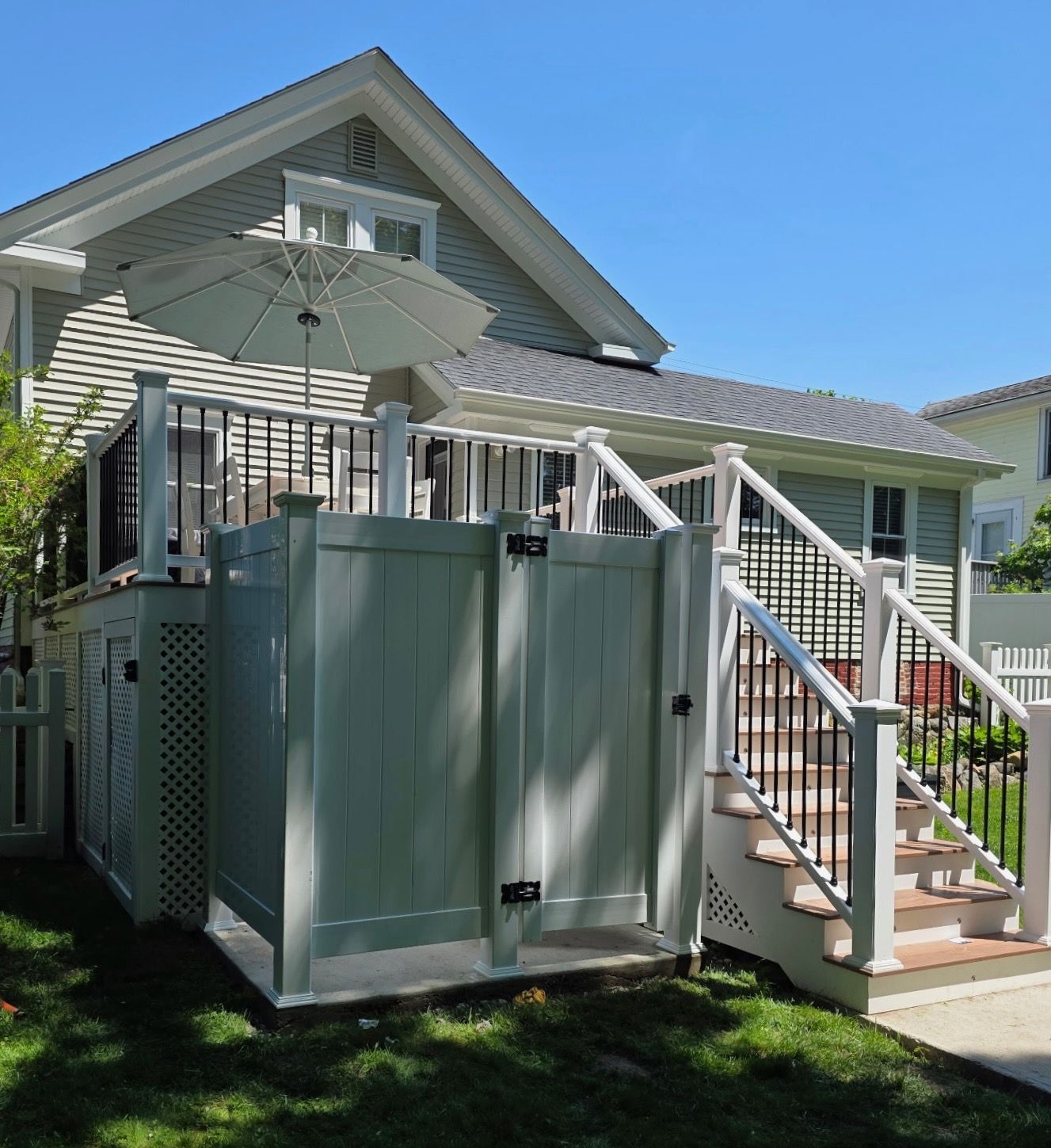 House porch with white railing, gray storage shed, and patio umbrella in a sunny yard