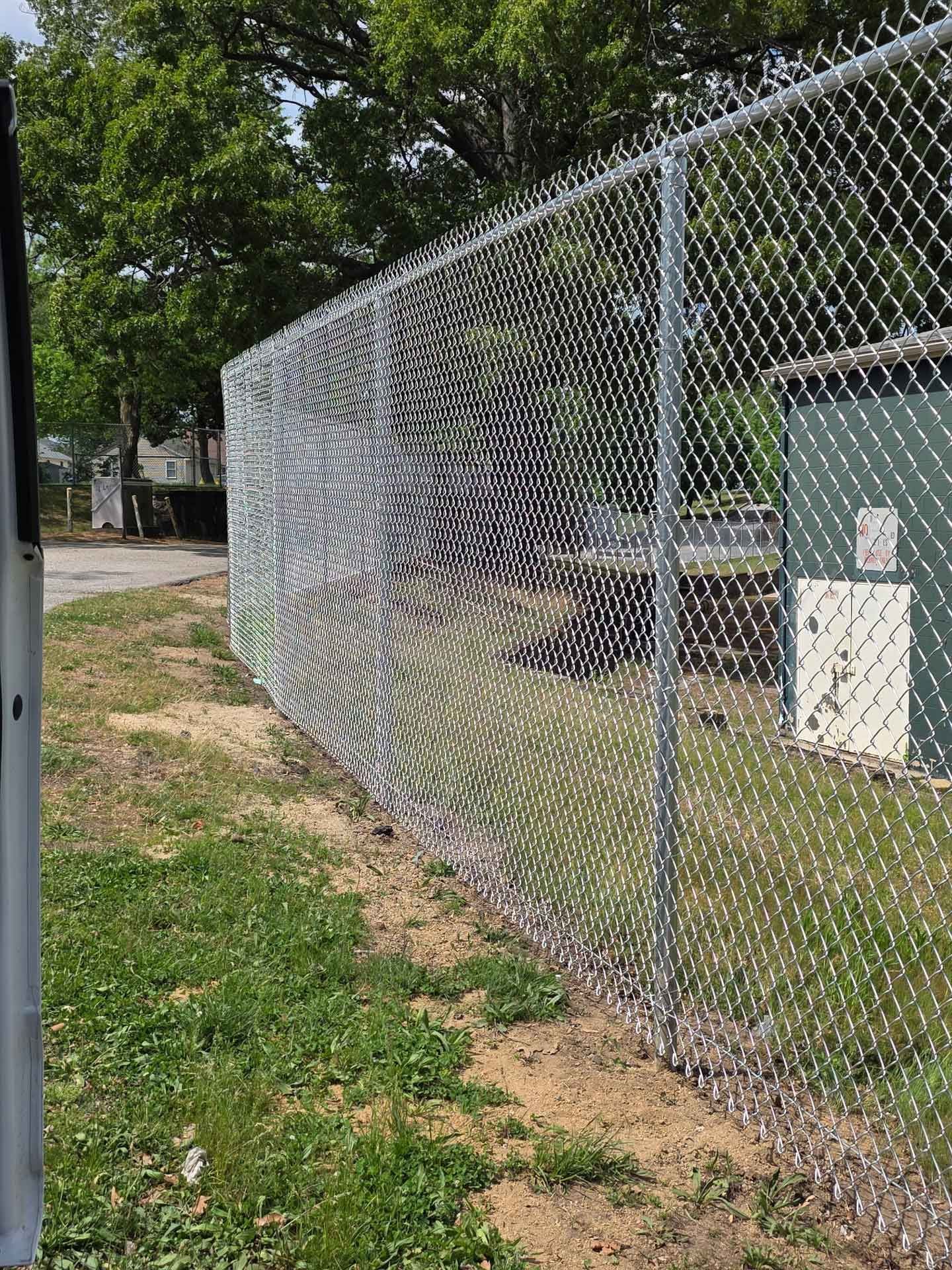 Chain-link fence beside a grassy path in a wooded outdoor area