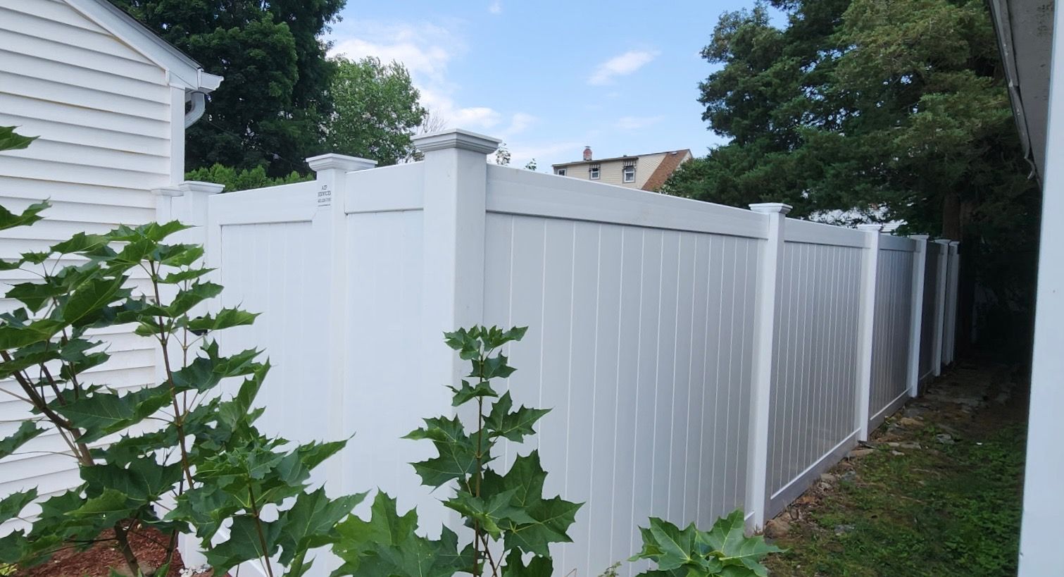 White vinyl privacy fence along a narrow side yard beside a house and trees
