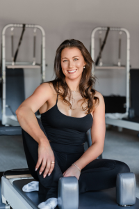 A woman is sitting on a pilates machine and smiling.