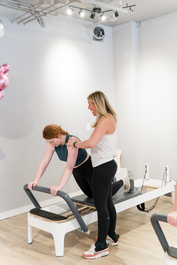 A woman is helping another woman on a pilates machine.