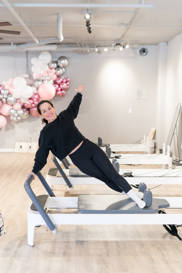 A woman is doing a side plank on a pilates machine in a gym.