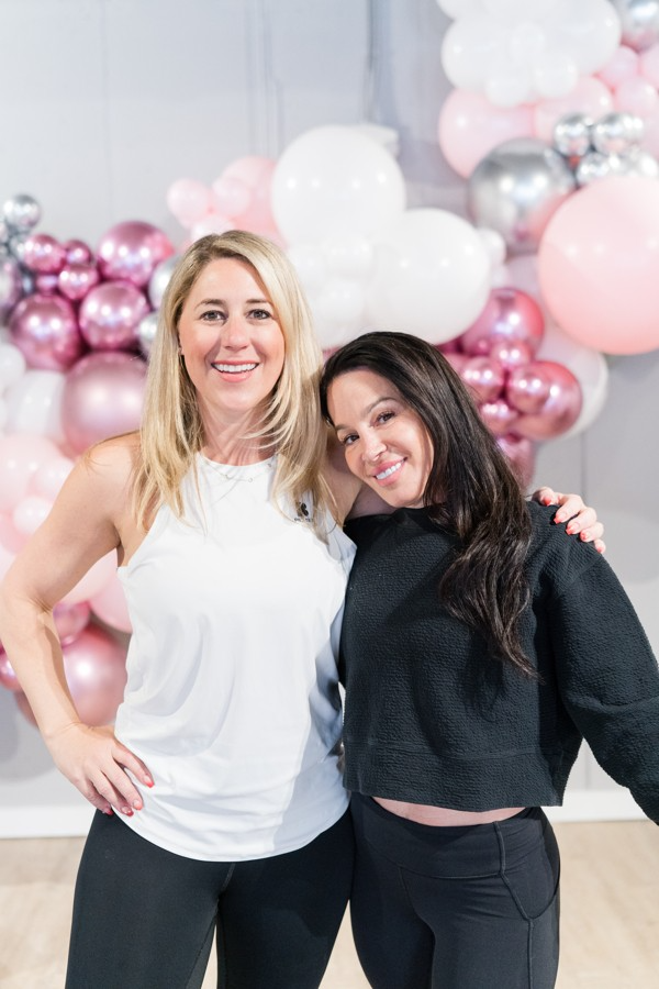Two women are posing for a picture in front of balloons.