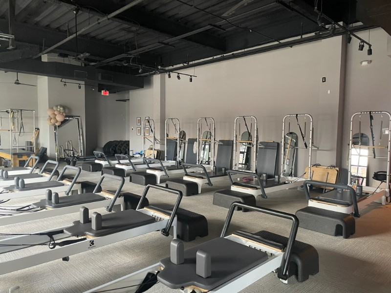 Pilates studio with rows of reformers, gray walls, and black ceiling.