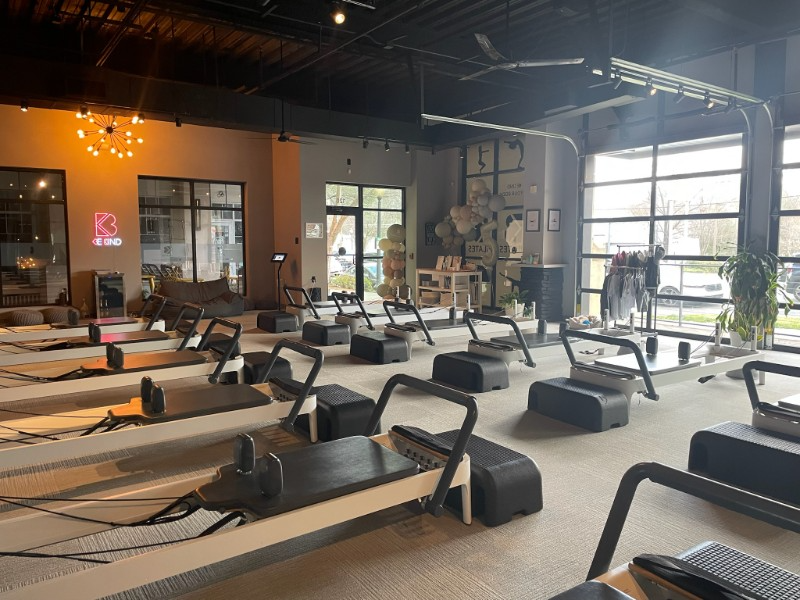 Pilates studio with reformers, neutral tones, large windows, and a chandelier.