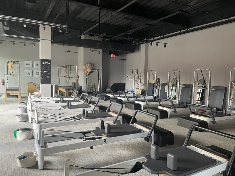 Pilates studio with several reformer machines in rows. Light gray walls and ceiling.