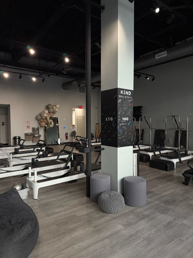 Pilates studio interior with exercise equipment, neutral colors, and column with logo.